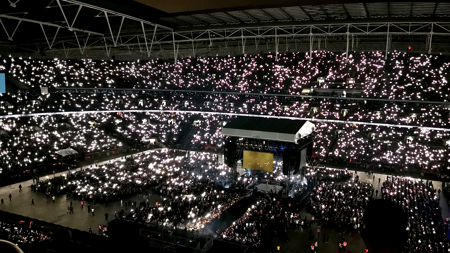 A wide shot of Wembley Stadium during AEW All In 2023, showing the fans lighting up the stadium with their torches