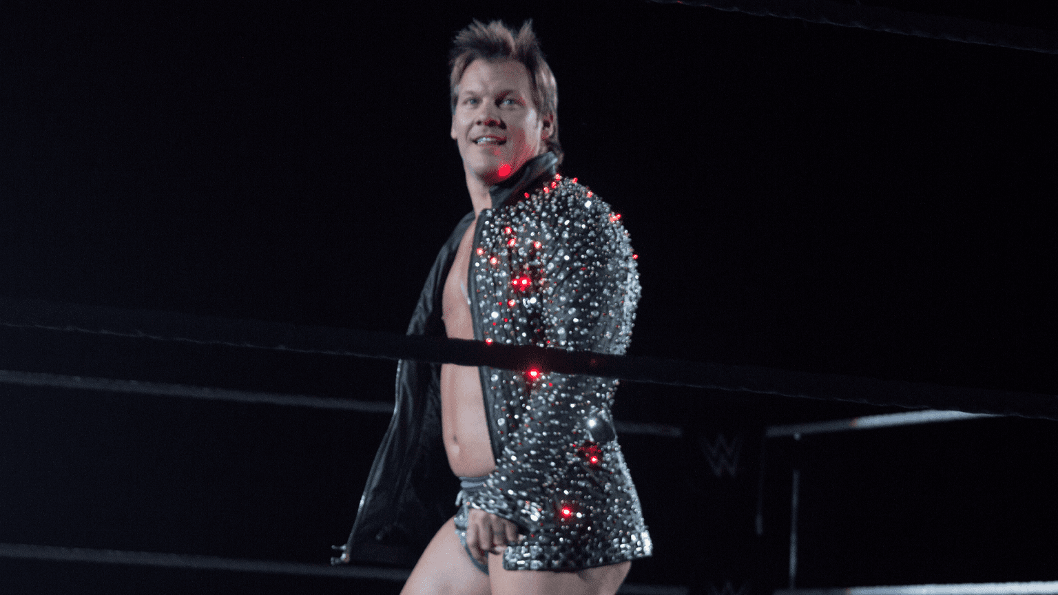 Chris Jericho in his light up jacket standing in a WWE ring with a dark backdrop.